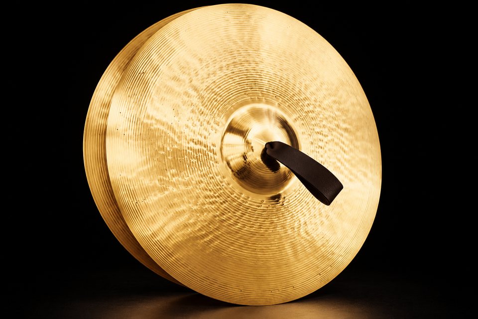 A pair of bright bronze orchestral crash cymbals with a leather strap